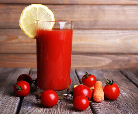 Glass of tomato juice with lemon and fresh tomatoes on wooden table on wooden wall backgroundの写真素材