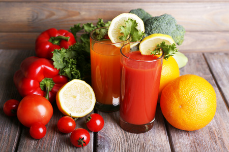 Carrot and tomato juice in glasses and fresh vegetables on wooden table on wooden wall backgroundの写真素材