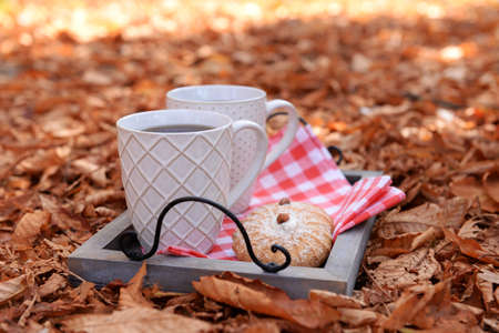 Cups of tasty hot drink and fresh cookies on tray, on autumn leaves backgroundの写真素材