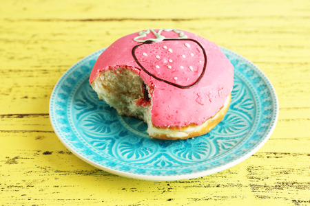 Bitten delicious donut on plate on wooden table close-upの写真素材
