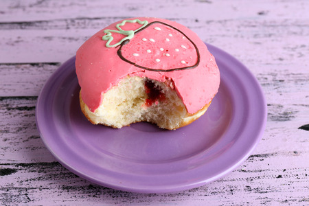 Bitten delicious donut on plate on wooden table close-upの写真素材