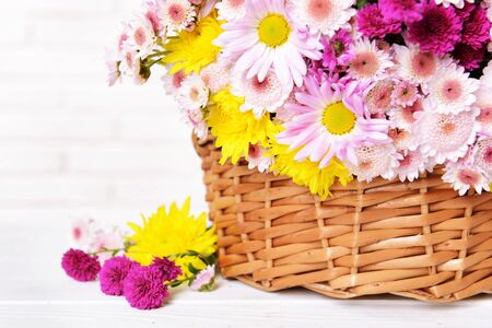 Beautiful flowers in wicker basket on table on light backgroundの写真素材
