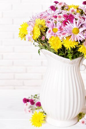 Beautiful flowers in pitcher on table on light backgroundの写真素材