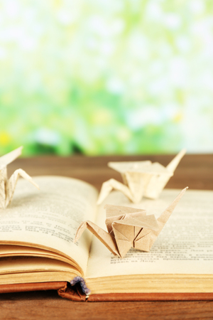 Origami cranes on old book on wooden table, outdoorsの写真素材