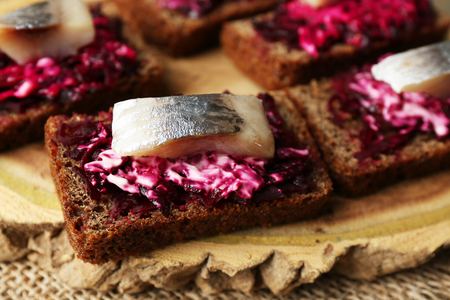 Canape herring with beets on rye toasts, on wooden board, on wooden table backgroundの写真素材