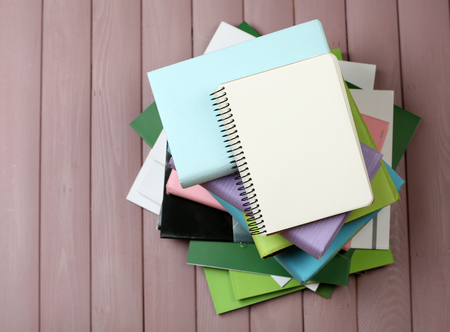 Notebook on top of pile of books and magazines on wooden background