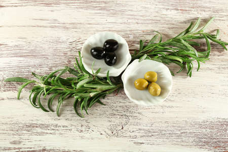 Two small plates with black and green olives and branches on painted wooden backgroundの写真素材