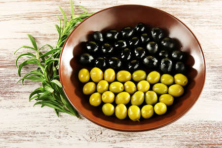 Black and green olives in bowl with branch on painted wooden backgroundの写真素材