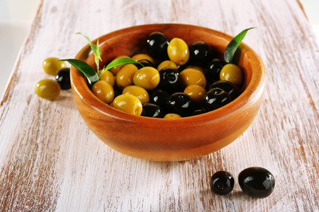 Black and green olives with leaves in bowl on painted wooden backgroundの写真素材