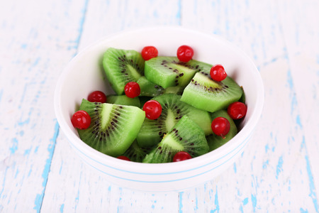 Bowl of slices kiwi with currants on color wooden backgroundの写真素材