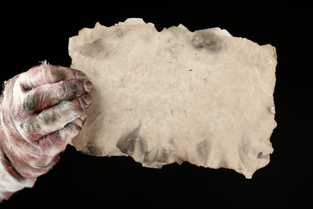 Hand of mummy holding old paper isolated on blackの写真素材