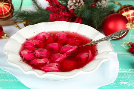 Traditional polish clear red borscht with dumplings and Christmas decorations on color wooden table backgroundの写真素材