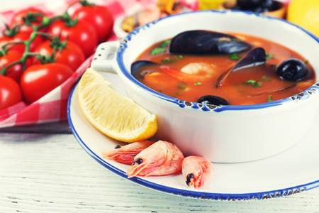 Tasty soup with shrimps, mussels, tomatoes and black olives in bowl on wooden backgroundの写真素材