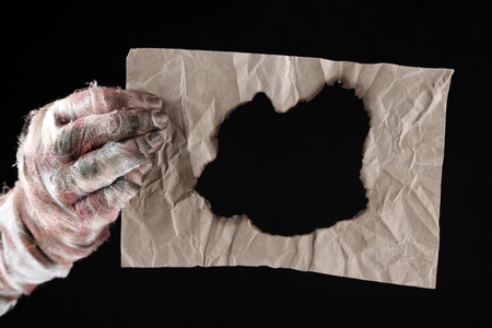 Hand of mummy holding old paper isolated on black