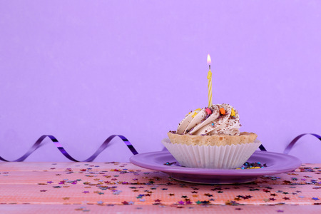 Birthday cup cake with candle with sparkles on plate on color wooden table and light backgroundの写真素材