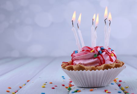 Birthday cup cake with candles and sparkles on color wooden table and light backgroundの写真素材