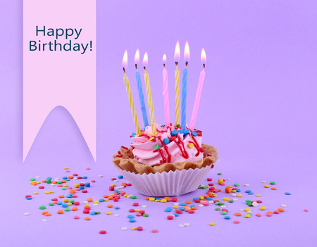 Birthday cup cake with candles and colorful sparkles on purple backgroundの写真素材
