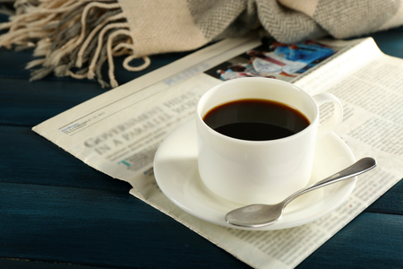 Cup of coffee with saucer and spoon on newspaper on color wooden backgroundの写真素材