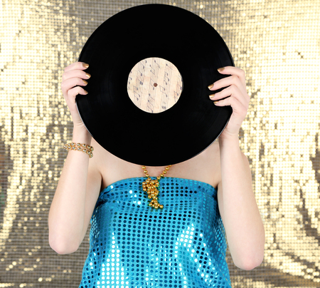 Young woman holding retro record in front of face, on shiny backgroundの写真素材