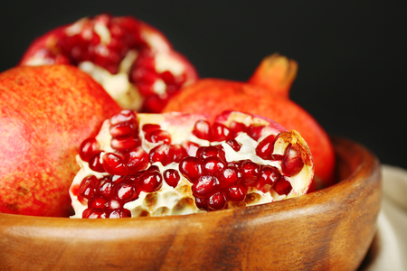 Juicy ripe pomegranates in wooden bowl, on dark backgroundの写真素材