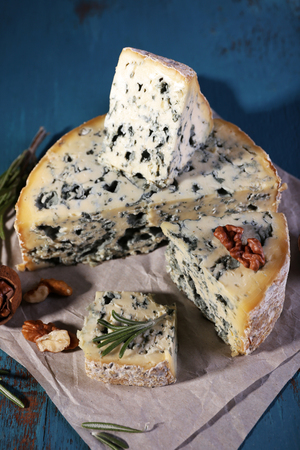 Blue cheese with sprigs of rosemary and nuts on sheet of paper and color wooden table backgroundの写真素材