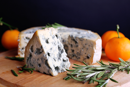 Blue cheese with sprigs of rosemary and oranges on wooden board and dark backgroundの写真素材