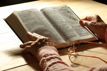 Hands of old woman with Bible on table and dark background