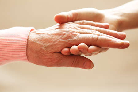 Old and young holding hands on light backgroundの写真素材