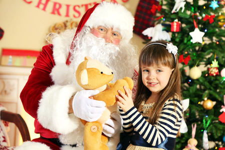 Santa Claus giving  present to  little cute girl near Christmas tree at homeの写真素材
