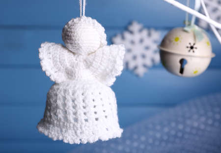 Knitted Christmas angel hanging on bud on color wooden background の写真素材