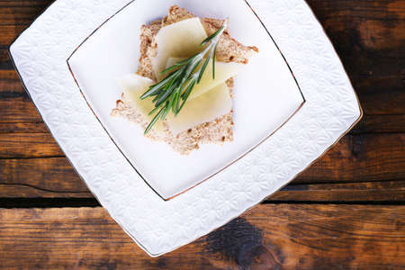 Crispbread with slices of Parmesan cheese with sprig of rosemary on plate on wooden table background
