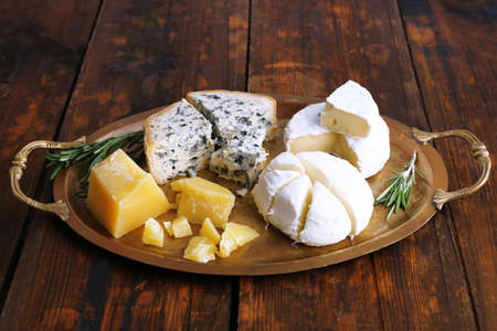 Different types of cheese on metal tray and wooden table background