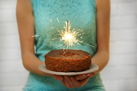 Woman holding tasty cake with sparkler, on grey wall backgroundの写真素材