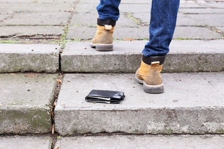 Lost leather wallet and walking male legs, outdoors