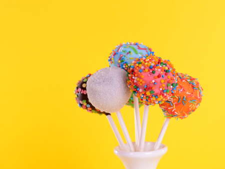 Sweet cake pops in vase on yellow backgroundの写真素材