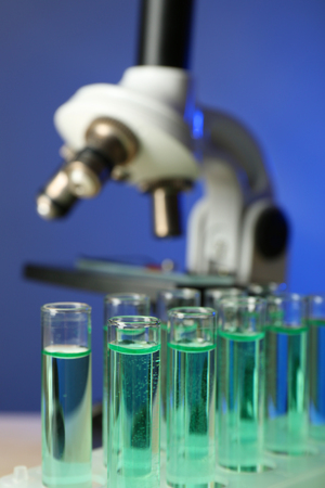 Microscope and test tubes on table, on color background