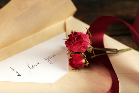 Envelope with love letter, vinous ribbon and dried rose on rustic wooden table backgroundの写真素材