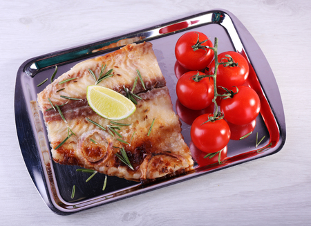 Dish of Pangasius fillet with rosemary and lime on metal tray and color wooden table background