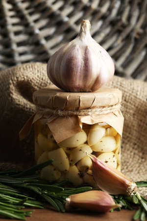Canned garlic in glass jar and wicker mat and rosemary branches, on wooden backgroundの写真素材