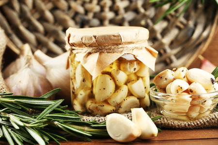 Canned garlic in glass jar and wicker mat and rosemary branches, on wooden backgroundの写真素材