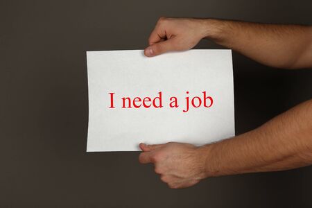 Sheet of paper with inscription I need a job in male hands on dark background