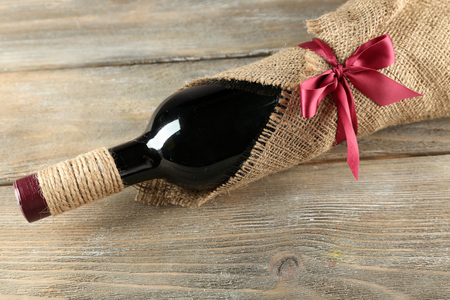 Red wine bottle wrapped in burlap cloth on wooden planks backgroundの写真素材