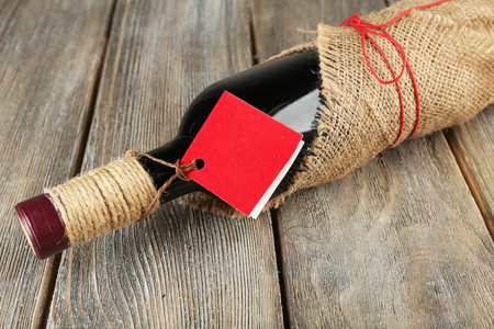 Red wine bottle wrapped in burlap cloth on wooden planks backgroundの写真素材