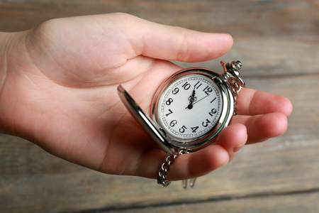 Silver pocket clock in hand on wooden backgroundの写真素材