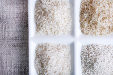 Different types of rice on plate on fabric background