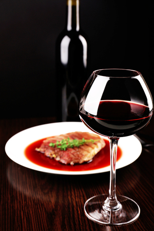 Glass of wine with grilled steak in wine sauce on dark backgroundの写真素材