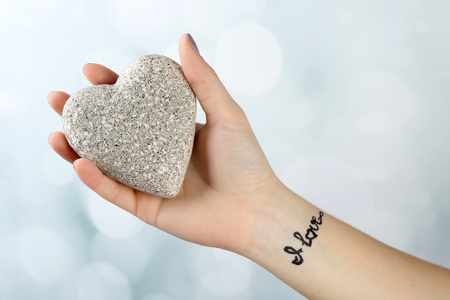 Female arm with tattoo holding decorative heart on light backgroundの写真素材