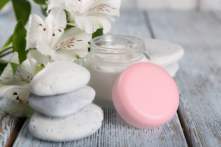 Cosmetic cream with flowers and spa stones on wooden backgroundの写真素材