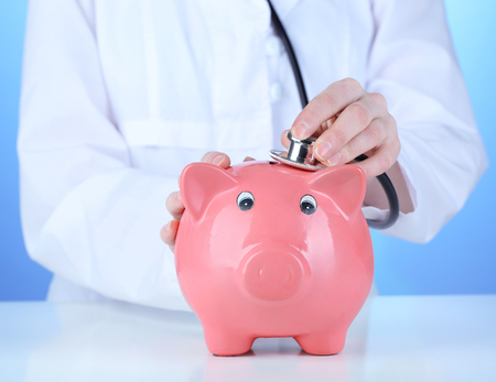 Doctor with pink piggy bank on blue background, close upの写真素材