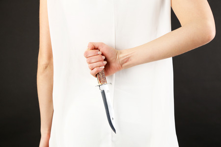 Woman holding knife behind her back on gray backgroundの写真素材
